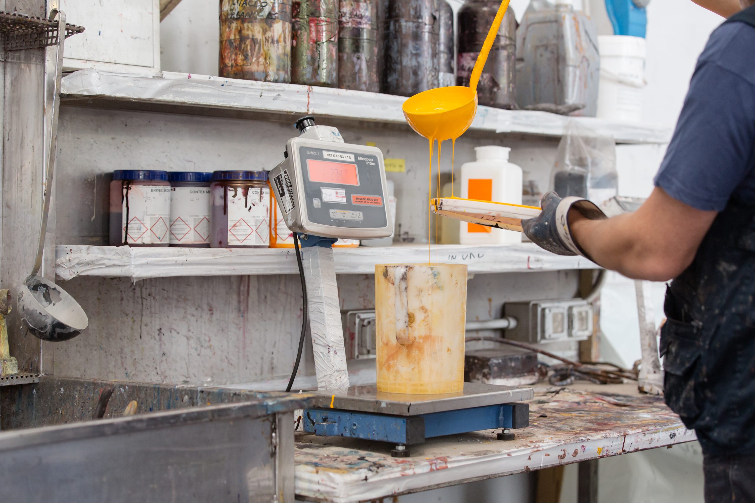 Worker weighing materials on an industrial scale in a production workshop, with containers and equipment on the workbench.