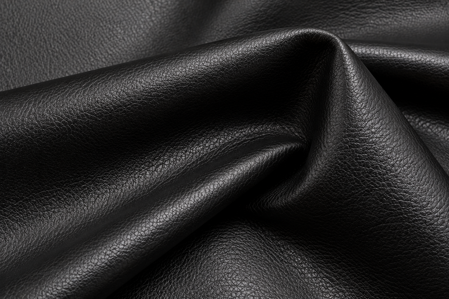 Close-up of black faux leather showing its smooth surface, subtle grain texture and reflective finish.