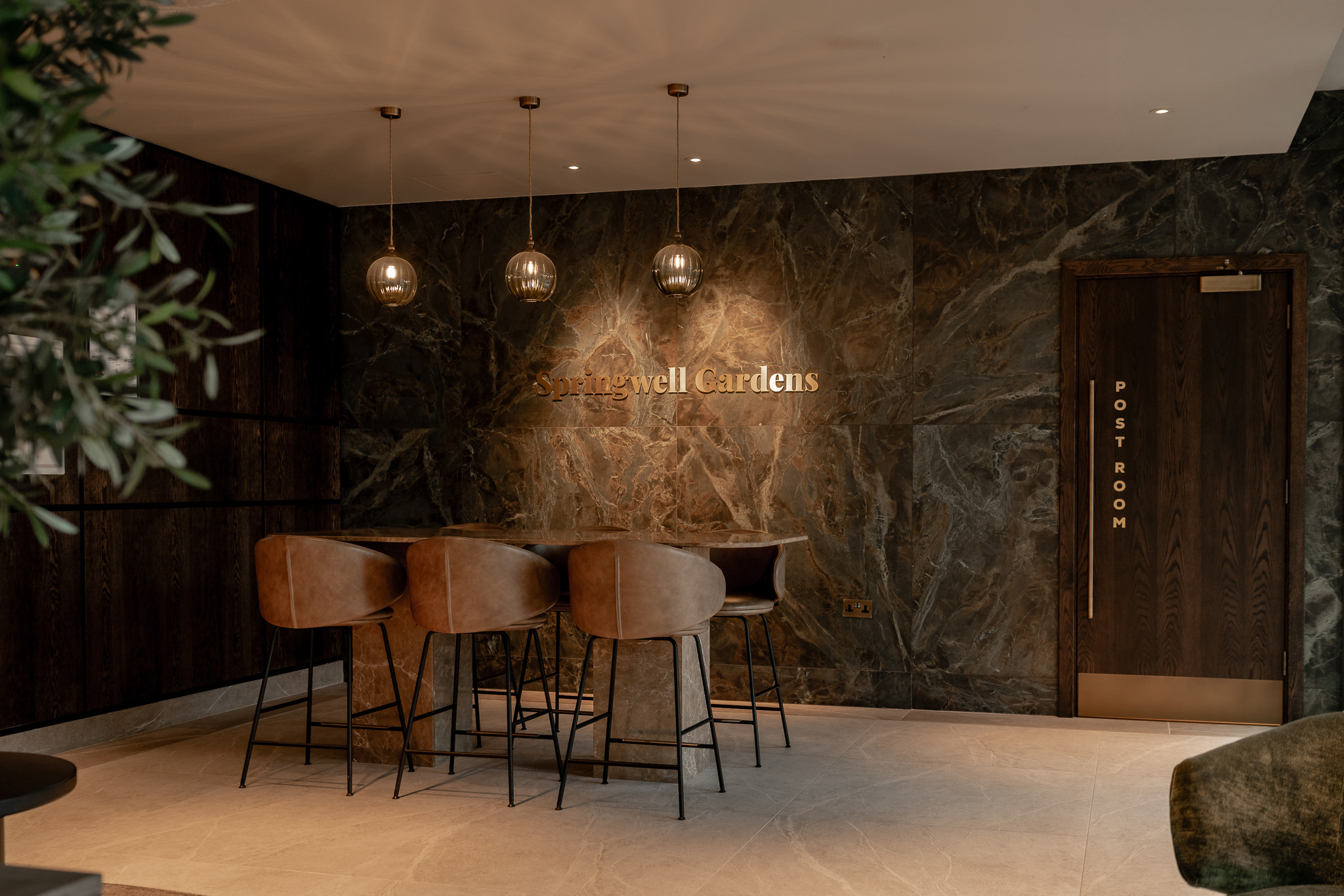 Warm, contemporary bar interior featuring leather-upholstered stools, dark textured walls and pendant lighting.